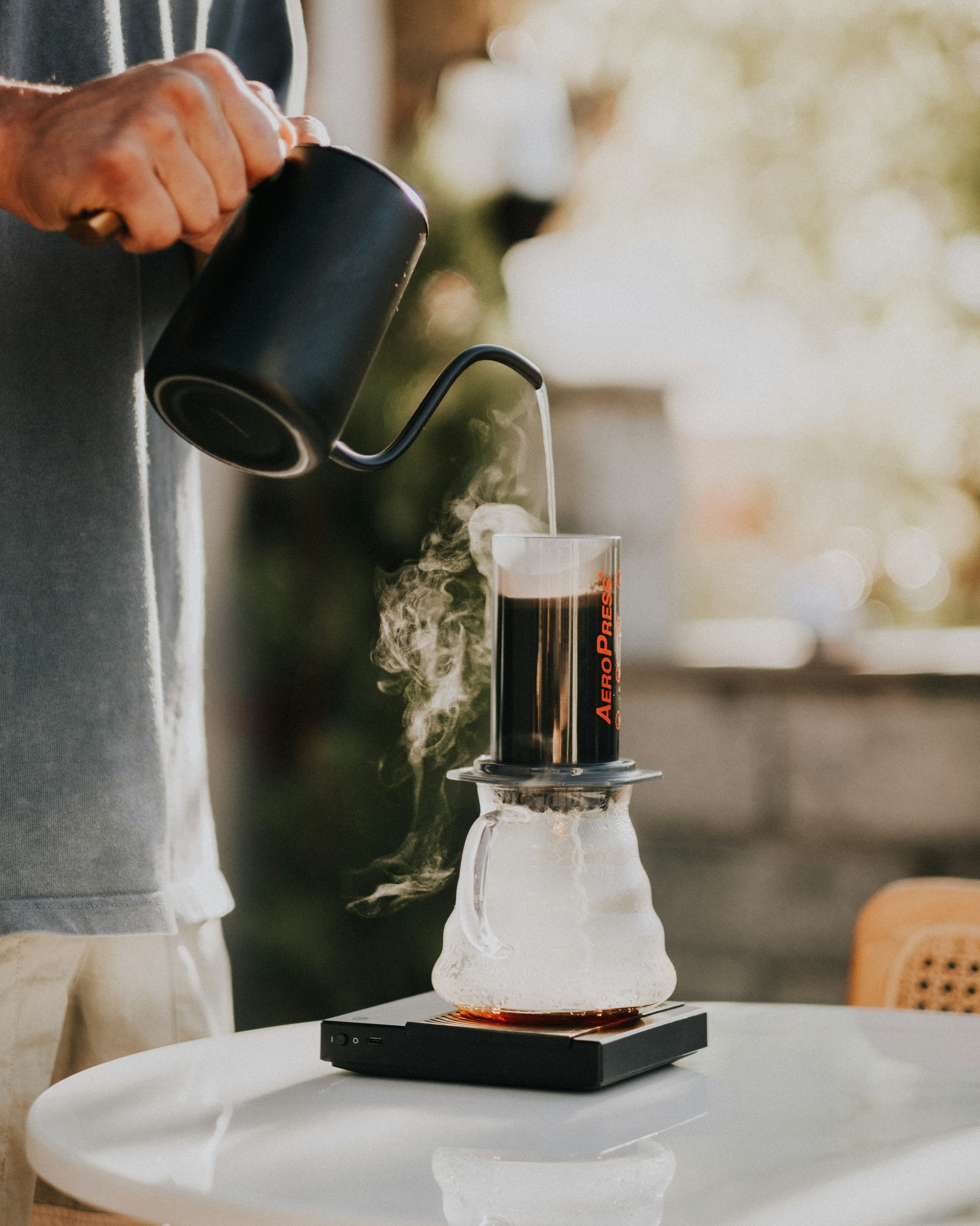 A man brews a coffee with an aeropress by pouring hot water with a gooseneck kettle onto the bed of coffee.