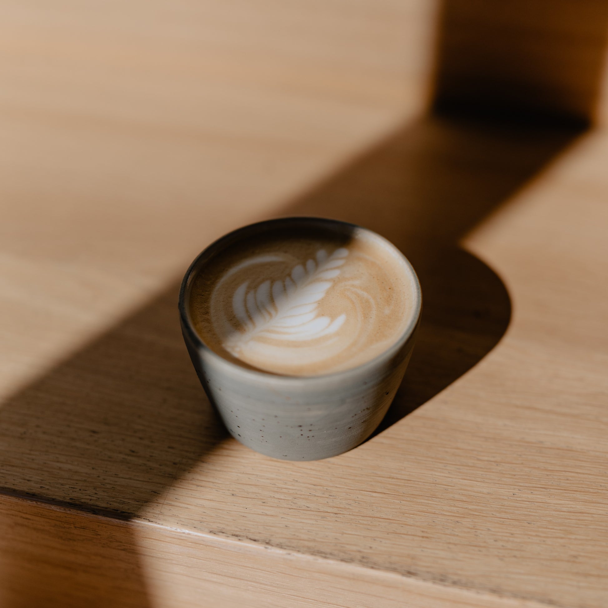 A iaro mug filled with a cappuccino with delightful latte art standing on a wooden surface. The lighting is warm but dramatic.