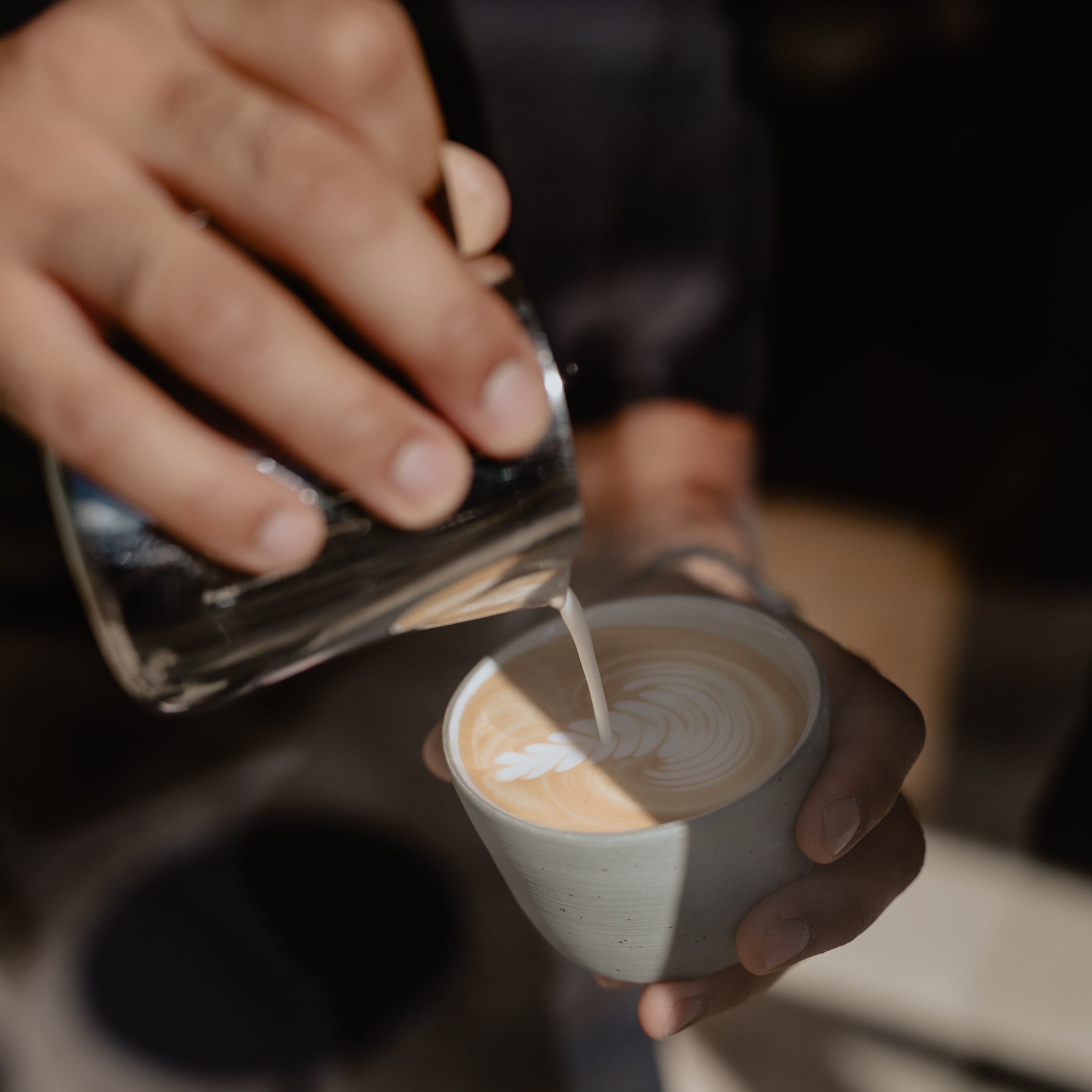 A small stream of milk is flowing out of the milk pitcher completing the intricate rosetta artwork.