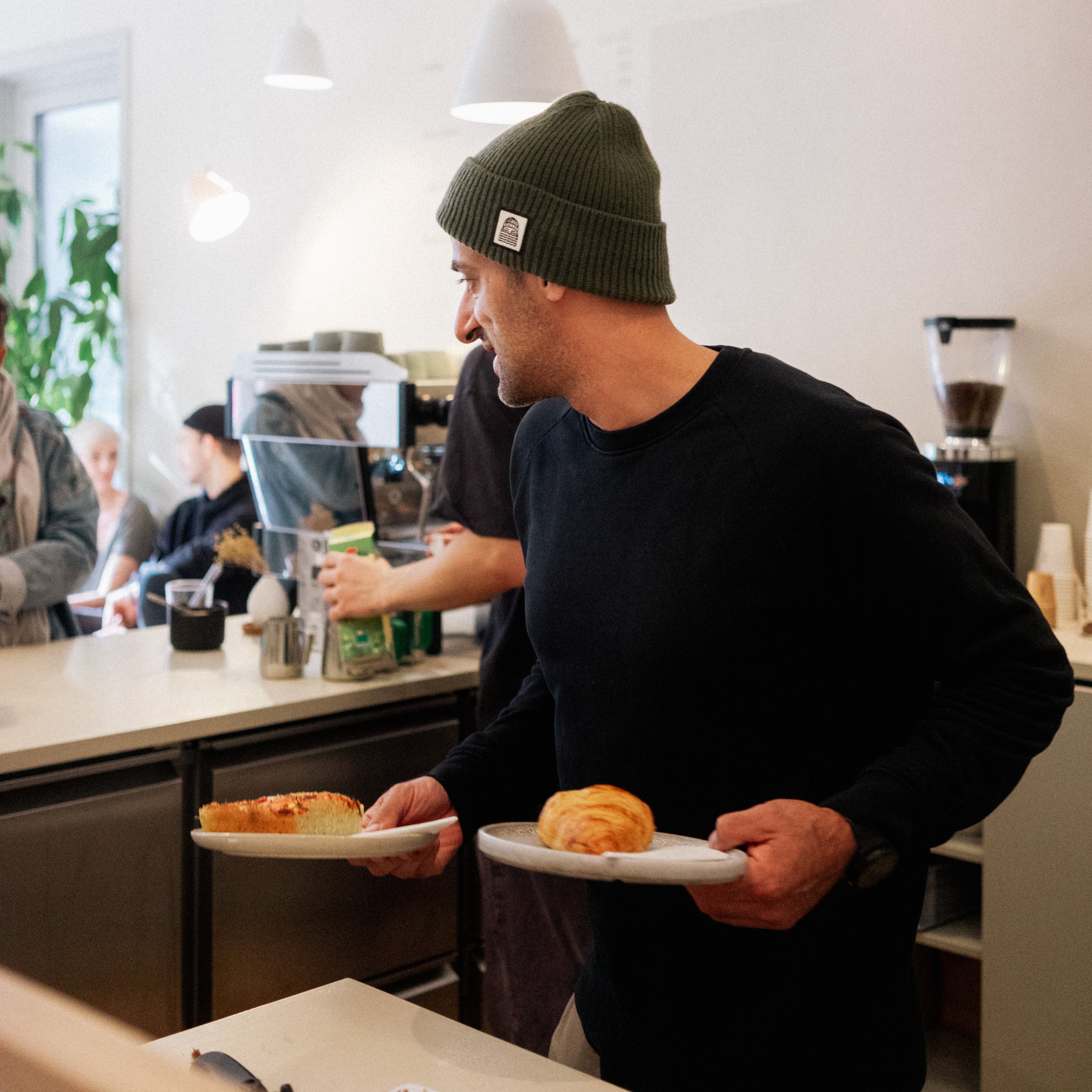 Co founder Armin Zandieh is holding a plate with a piece of focaccia and one with a crossaint, getting ready to serve them to his guests.