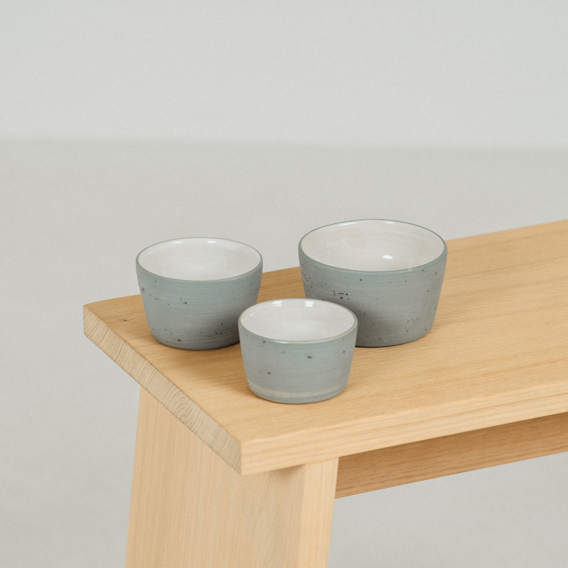 All three sizes of the blue-grey iaro specialty coffee mug are place on a ractangular wooden stool