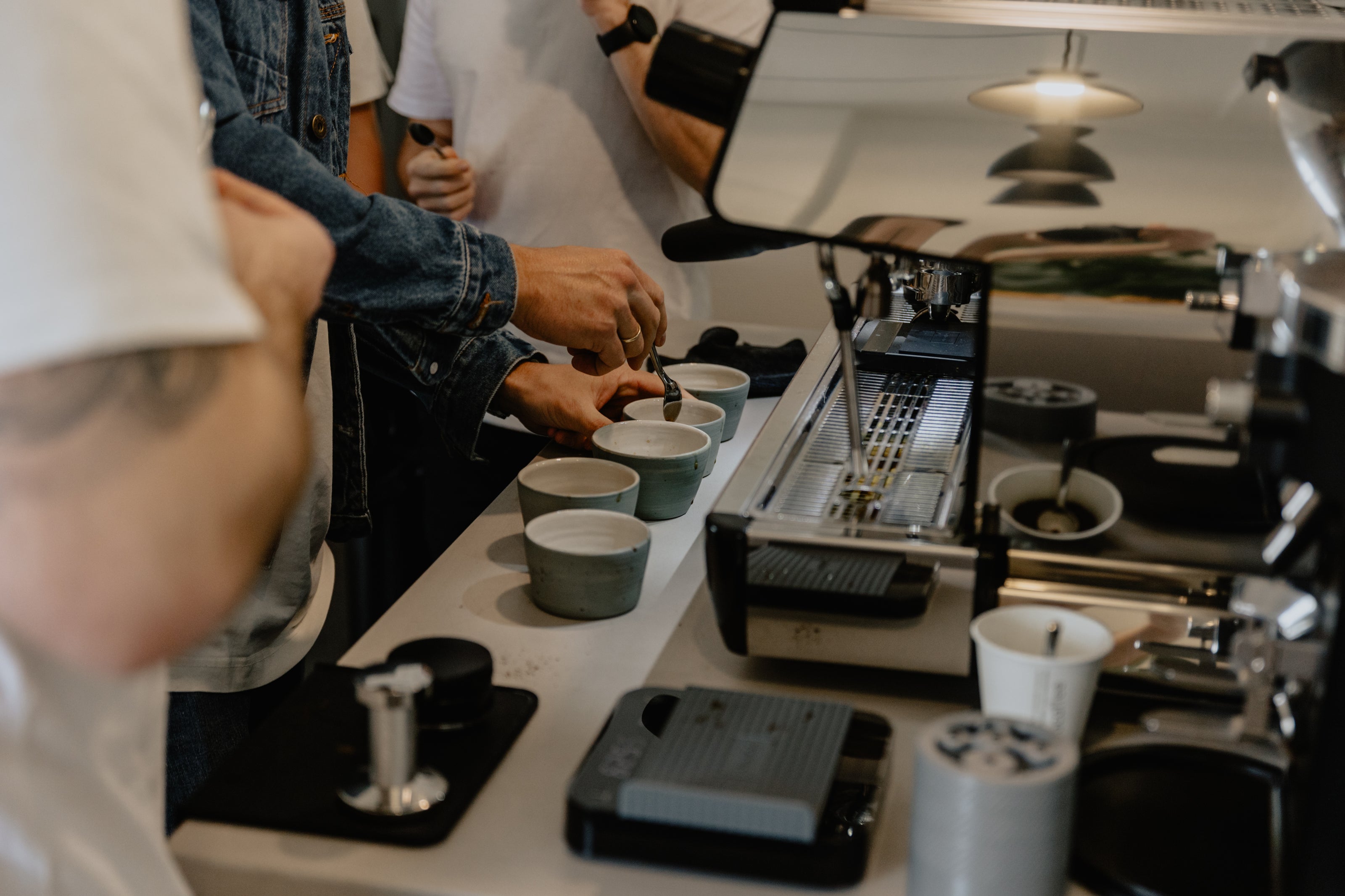 Barista workshop with espresso machine, coffee mugs, brewing equipment, and people