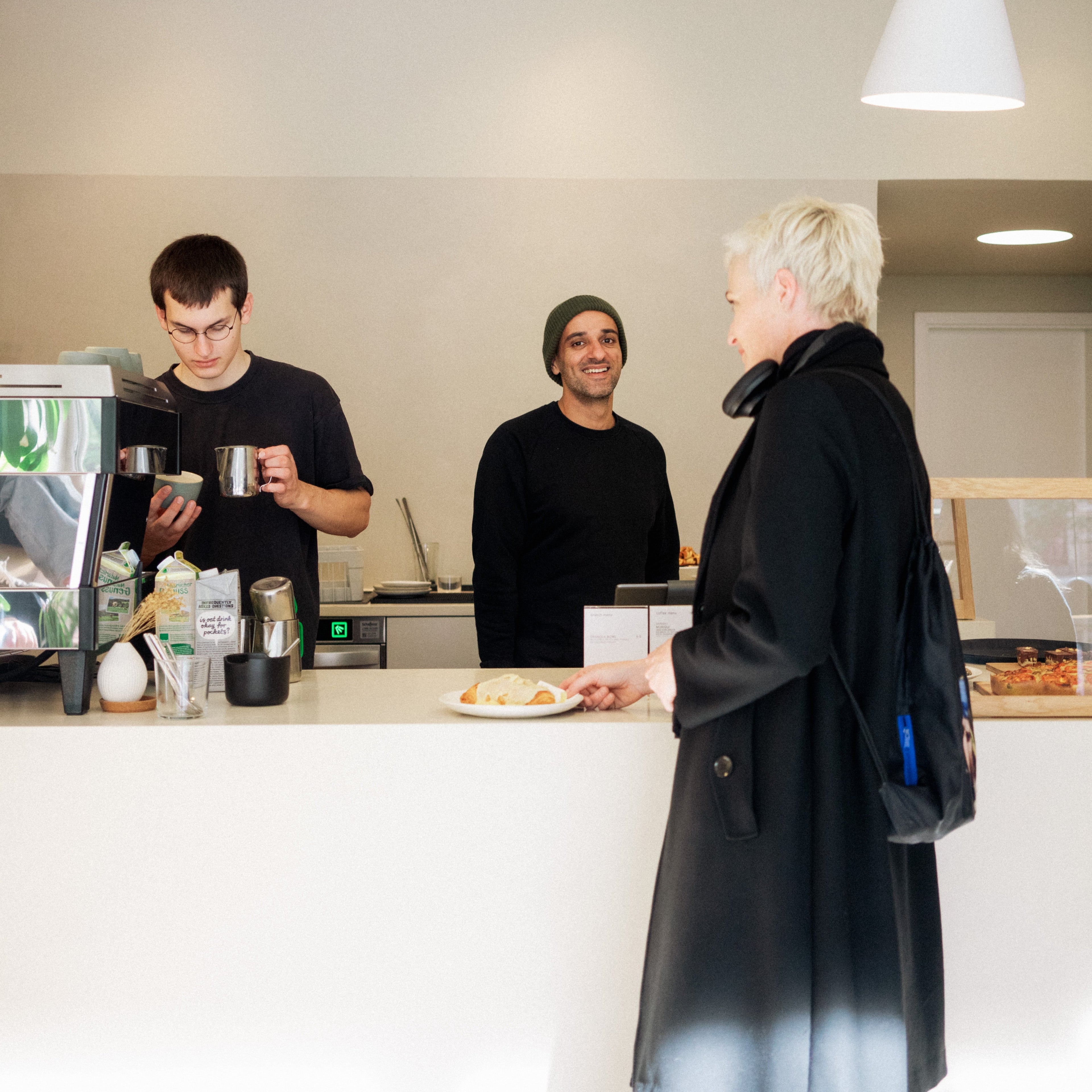 A barista and the founder of the iaro specialty roastery are standing behind the counter while a woman waits for her coffee.