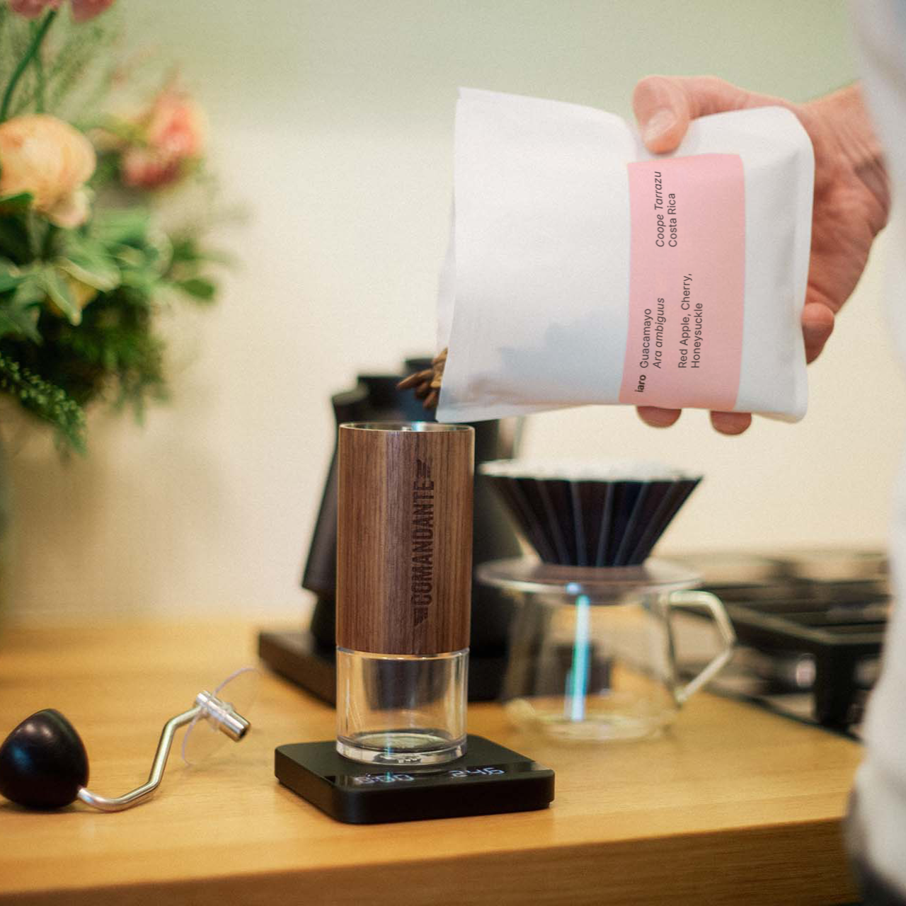 Specialty coffee beans are being poured into a Comandante hand grinder and weighed to prepare a filter coffee with the origami filter.