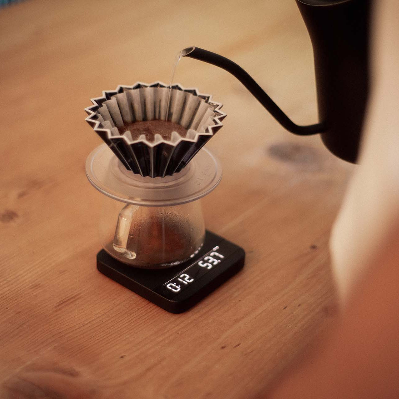 Hot water is slowly being poured onto an origami filter with a gooseneck kettle to prepare a fresh hand brew.