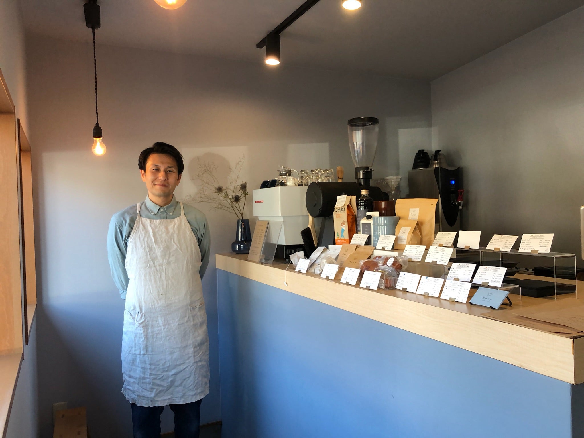 Man standing next to the counter in a japanese coffeeshop with different specialty coffees layed out on the counter next to a la Marzocco espresso machine