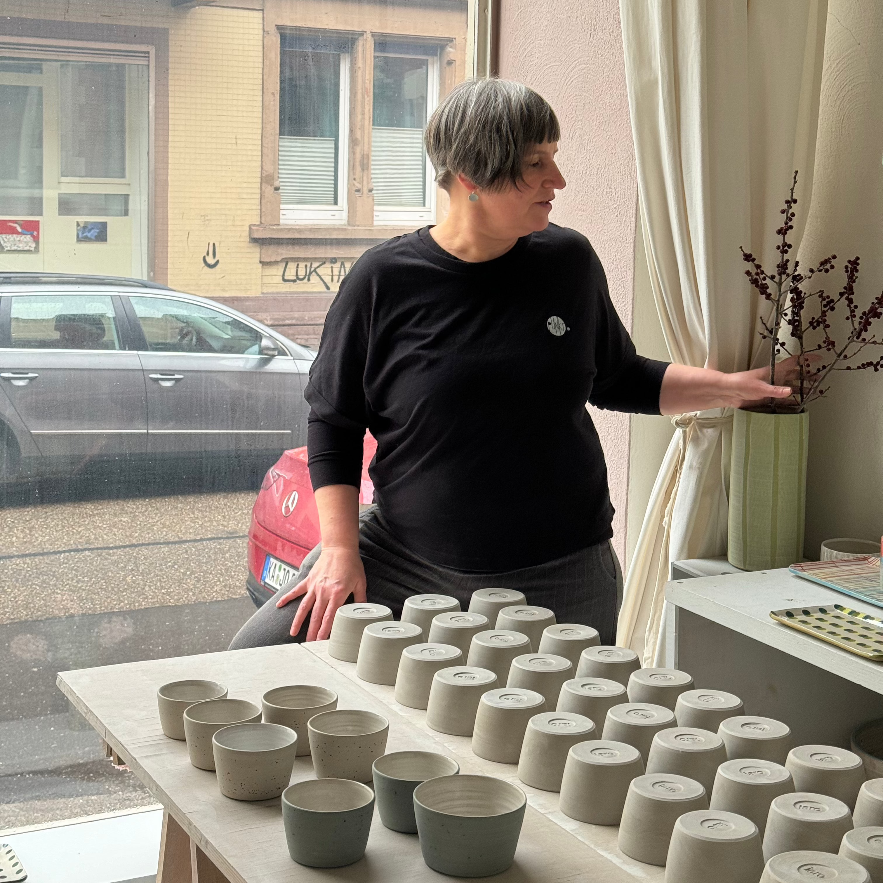 The artist Jutta Becker is standing besides a workbench in her atelier. The workbench is filled with iaro Mug specially made for specialty coffee.