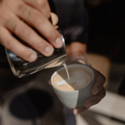 Latte art is being poured into a blue-grey specialty coffee cup.