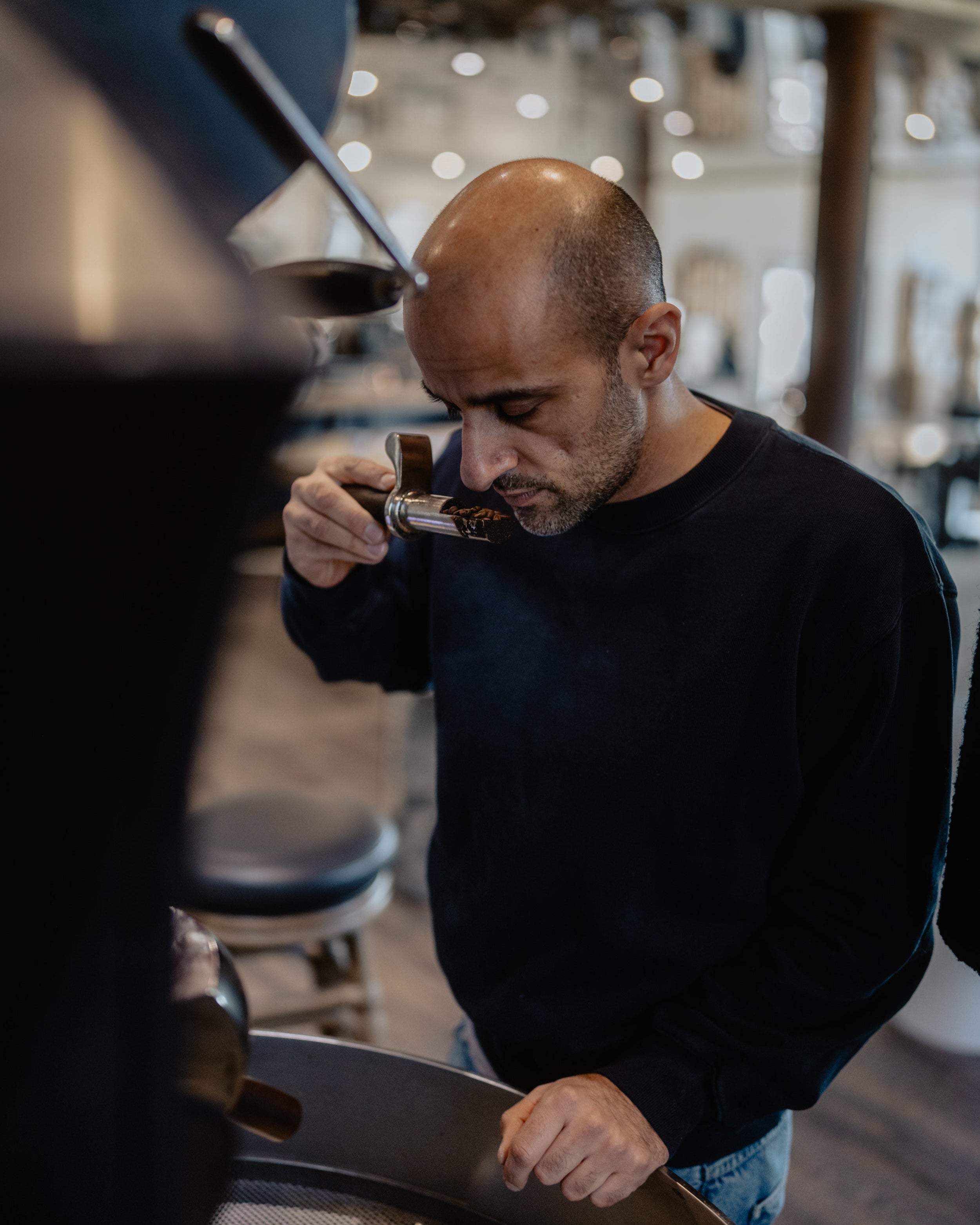 The founder of the iaro specialty coffee roastery is standing close to the roaster and is analyzing the smell of the freshly roasted beans.