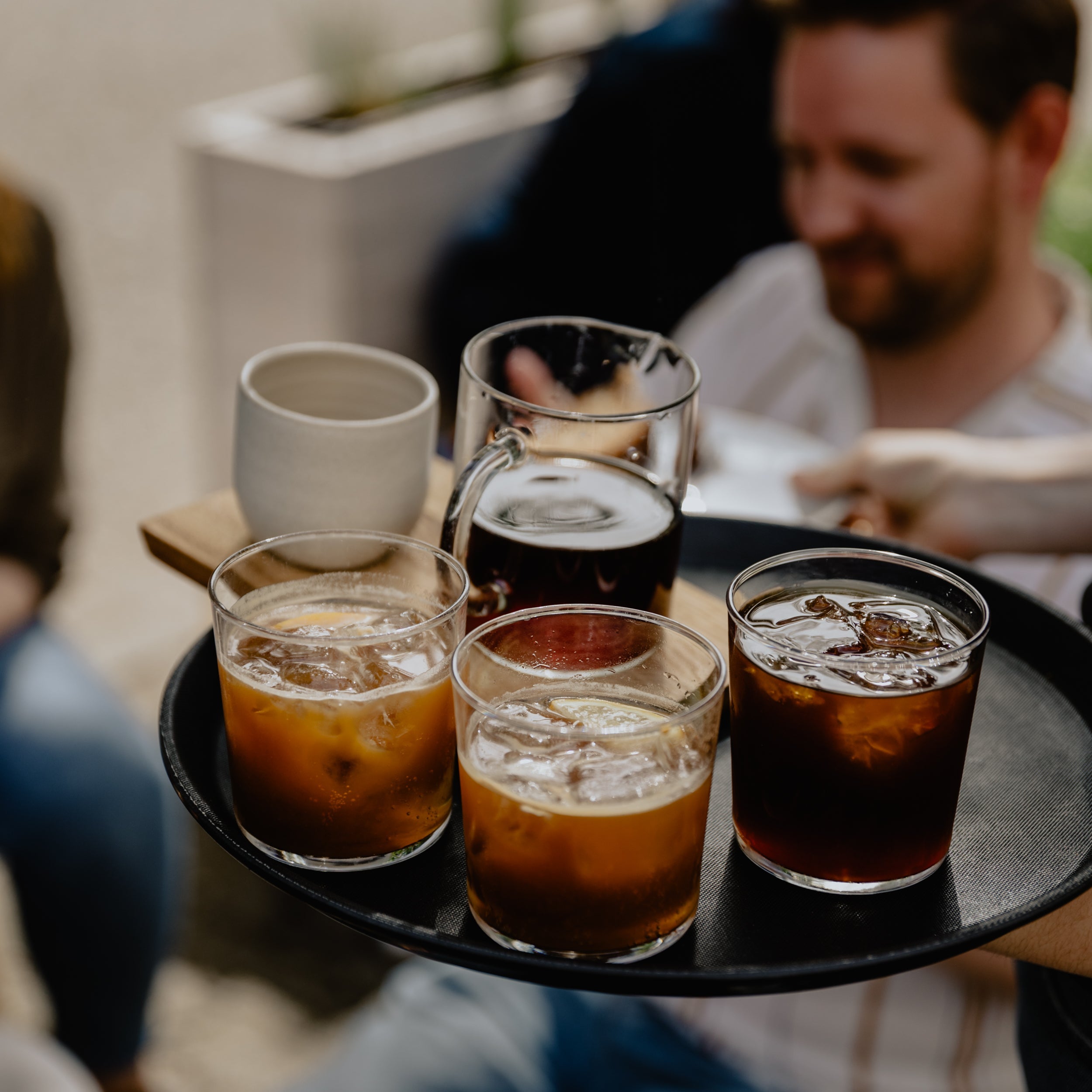 3 glasses of iced coffee drinks in simple glasses and a caraffe of hand brew on a black tray